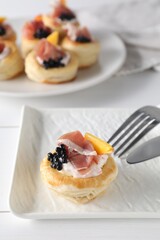Delicious puff pastry with cream cheese, ham, black caviar, peach and cutlery on white wooden table, closeup
