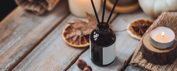 Home comfort, coziness, aromatherapy. Cozy interior with knitting, burning candles and aroma perfume diffuser in the living room. Fall scent, sweet pumpkin pie fragrance dry leaves, autumn mood banner
