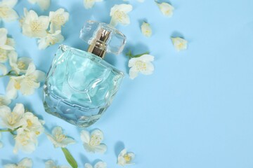 Aromatic perfume in bottle and beautiful jasmine flowers on light blue background, flat lay. Space for text