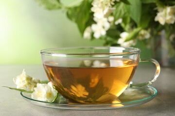 Aromatic jasmine tea in cup, flowers and green leaves on light grey table