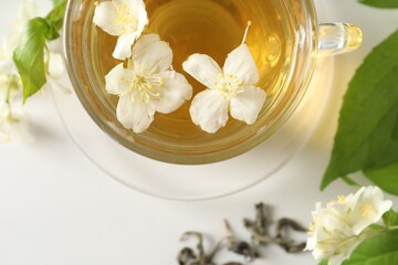 Aromatic jasmine tea in cup, flowers and leaves on white table, top view