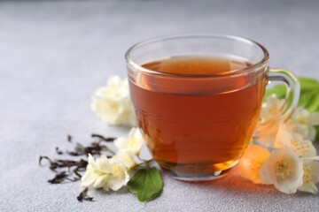 Hot jasmine tea in cup and flowers on light grey table
