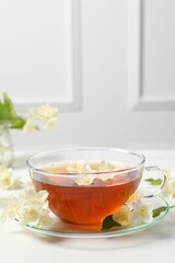 Hot jasmine tea in cup and flowers on white marble table, space for text