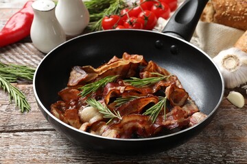 Delicious bacon slices in frying pan and products on wooden table, closeup