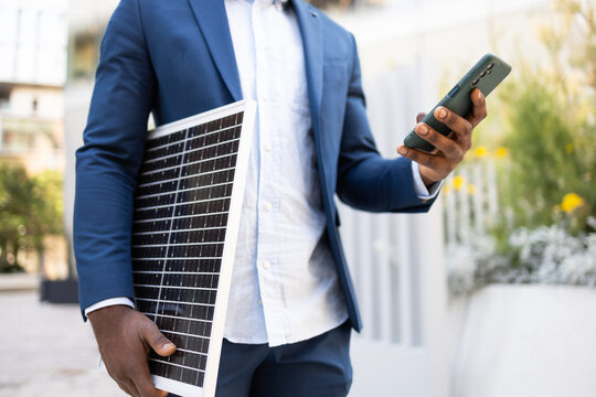 Anonymous businessman with solar panel using smartphone outdoors