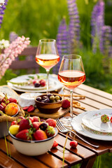 Beautiful elegant outdoor arrangement in meadow with purple blue lupins. Perfect date, private wedding or romantic marriage proposal. Summer, sunset, golden hour. Appetisers, rose wine, strawberry
