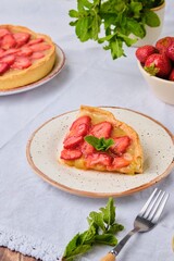 Sliced ​​round shortcrust tart filled with rhubarb, topped with slices of fresh strawberries and jelly on a ceramic plate. Rhubarb recipes.