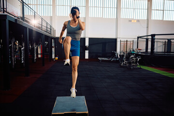 Female athlete jumping on  box while working out in health club.