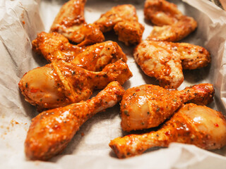 Asian style marinated chicken drumsticks and wings on cooking paper in a metal tray ready to be cooked. Fine poultry product for oven or barbecue. Simple popular traditionally meal.