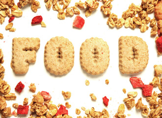 Word food with letters made from cookie on white background framed by granola cereal with dried strawberry. Top down view.