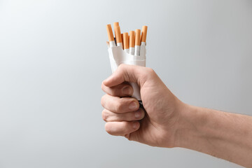 Stop smoking. Man holding pack with cigarettes on grey background, closeup