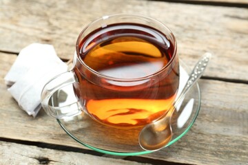 Aromatic tea in glass cup, spoon and teabags on wooden table