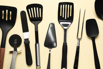 Different spatulas and other kitchen utensils on beige background, flat lay