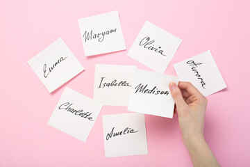 Woman holding paper stickers with name on pink background, top view. Choosing baby's name