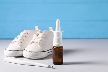 Child`s sneakers, thermometer and nasal spray on grey table, closeup. Space for text