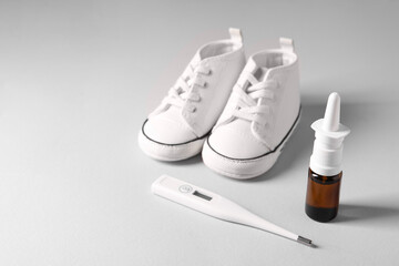 Child`s sneakers, thermometer and nasal spray on grey table, closeup. Space for text