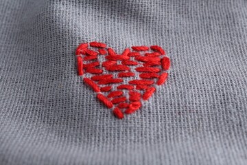 Fototapeta premium Embroidered red heart on gray cloth, above view