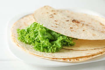 Tasty homemade tortillas and lettuce on white wooden table, closeup