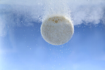 Effervescent pill dissolving in water on light blue background, closeup