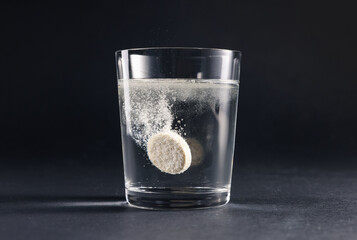 Effervescent pill dissolving in glass of water on grey table