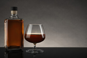 Bottle and glass with whiskey on table against gray background, space for text