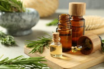 Essential oils in bottles and rosemary on light gray table, closeup
