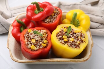 Quinoa stuffed bell peppers and basil in baking dish on white tiled table, closeup