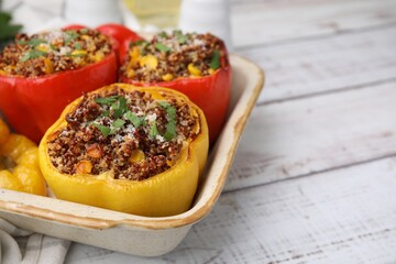 Tasty quinoa stuffed bell peppers with corn in baking dish on white wooden table, closeup. Space for text