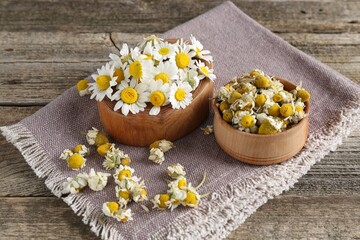 Dry and fresh chamomile flowers on wooden table