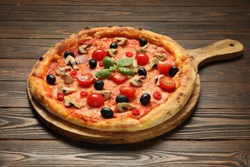 Delicious pizza with tomatoes, mushrooms, black olives and basil on wooden table