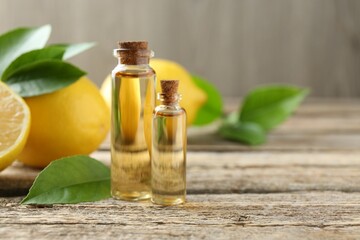 Essential oils in bottles, lemons and green leaves on wooden table, space for text