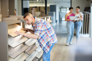 Obraz premium Interested casual young adult man thoughtfully evaluating eco-friendly wood grain laminate flooring options in building hypermarket, choosing perfect design for home renovation..
