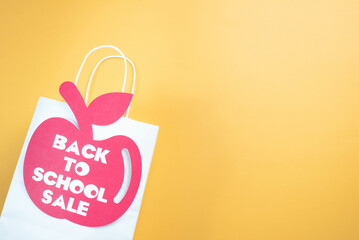 Back to school, apple shaped tag, on paper, shopping bag.  Yellow background.