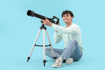 Young man looking at stars through telescope on blue background © Pixel-Shot
