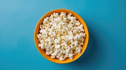 Popcorn in yellow bowl against blue background viewed from above