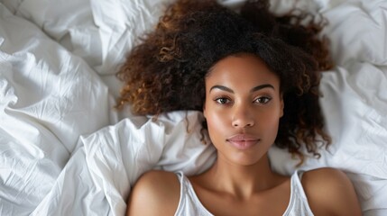 Tranquil biracial woman with curly hair relaxing on white bed, evoking themes of relaxation, self-care, wellness, and peaceful mornings.