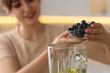 Young woman making delicious smoothie with blender in kitchen, selective focus