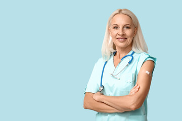 Mature female doctor with medical patch on arm against blue background. Vaccination concept