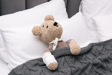 Toy cute bear with bandage and thermometer under blanket in bed