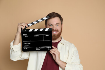 Making movie. Smiling man with clapperboard on beige background