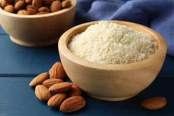 Fresh almond flour in bowl and nuts on blue wooden table, closeup