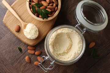 Fototapeta premium Fresh almond flour in jar, spoon and nuts on wooden table, flat lay