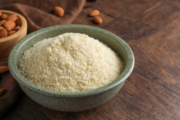Fresh almond flour in bowl and nuts on wooden table, closeup. Space for text
