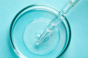 Glass pipette and petri dish with liquid on light blue background, top view