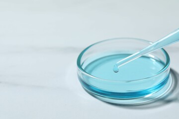 Dripping liquid from pipette into petri dish at white table, closeup. Space for text