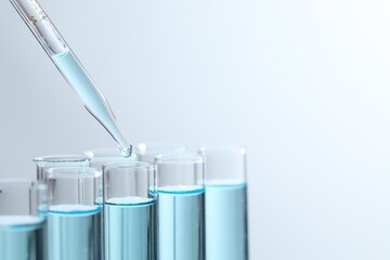 Dripping liquid from pipette into test tube on light background, closeup. Space for text
