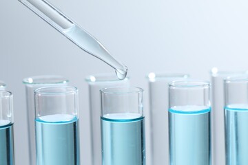 Dripping liquid from pipette into test tube on light background, closeup