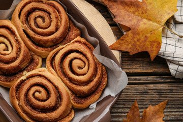 Baking dish of tasty cinnamon rolls and autumn leaves on wooden background