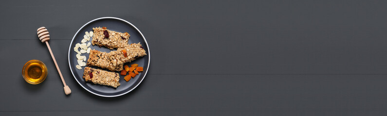 Tasty homemade granola bars with dried fruits and jar of honey on grey wooden table, flat lay. Banner design with space for text