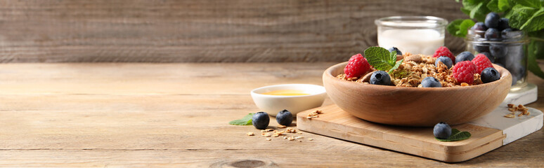 Tasty granola served with berries, honey and yogurt on wooden table. Banner design with space for text
